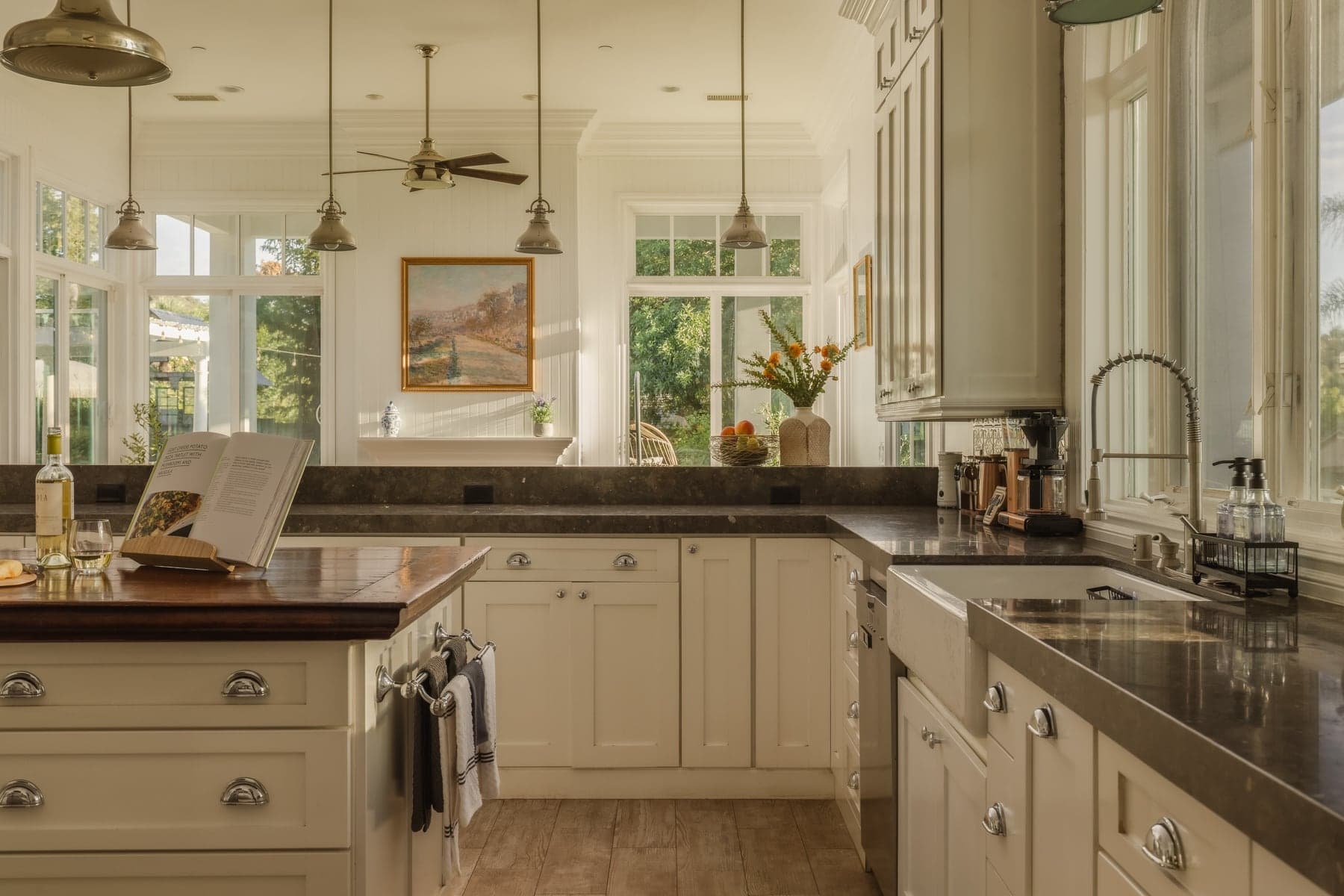 A kitchen seen from the working side of the counter, with an open cookbook and a window above the sink.