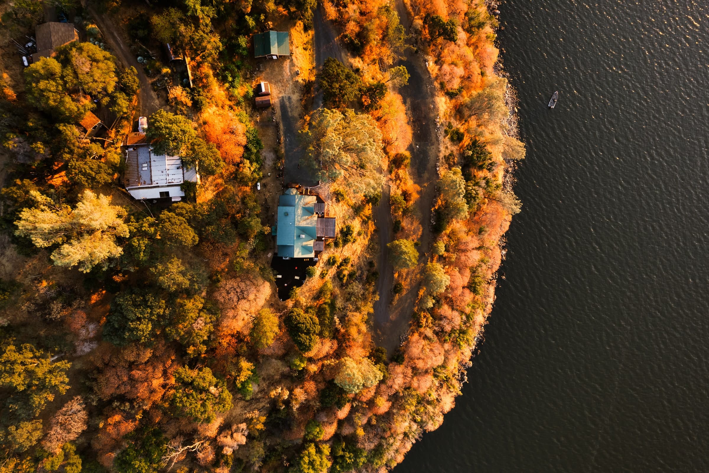 Aerial view of a lakeside home surrounded by autumn trees beside dark water