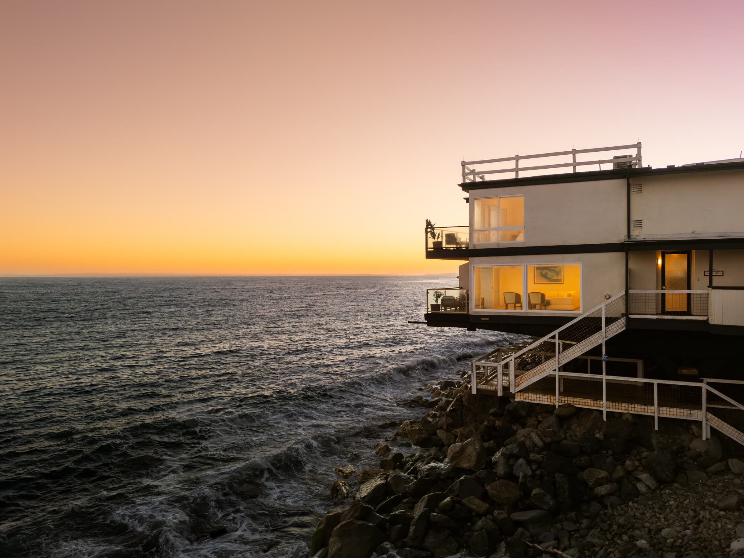 Modern house perched above the ocean at sunset with waves below
