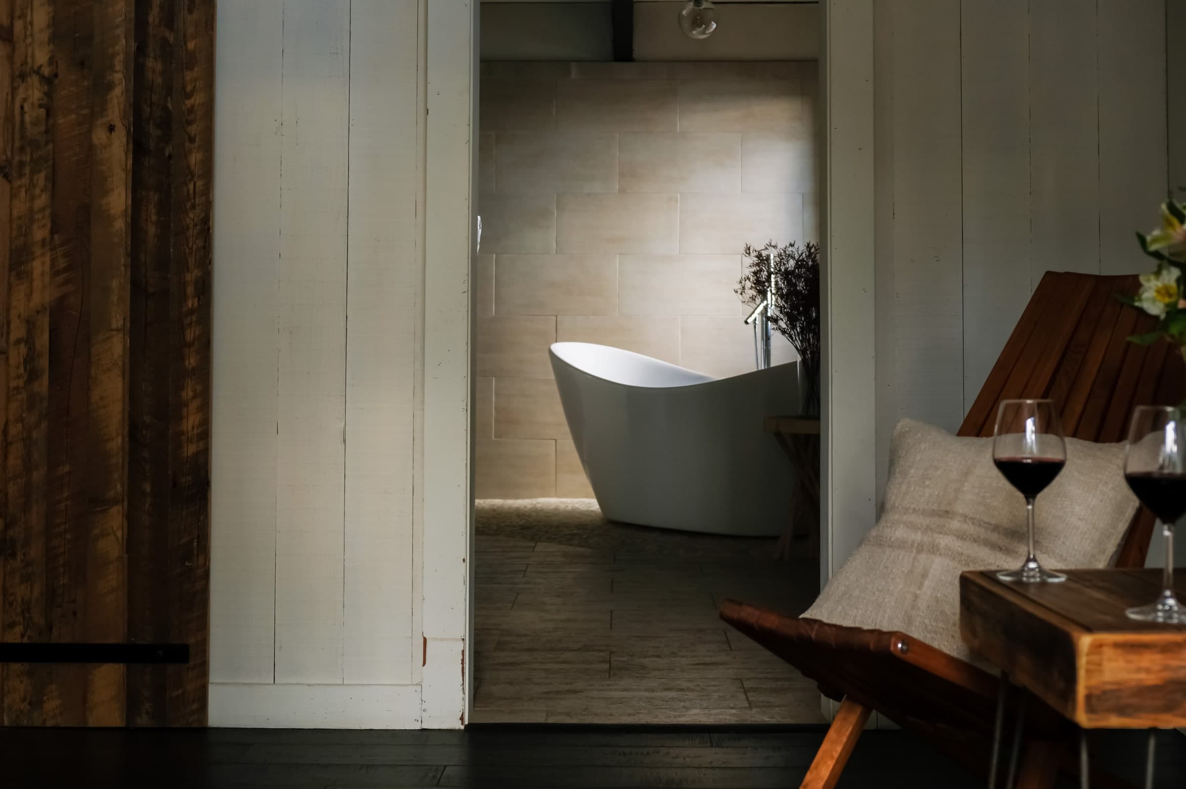 Freestanding soaking tub beyond a rustic dining table set with two wine glasses
