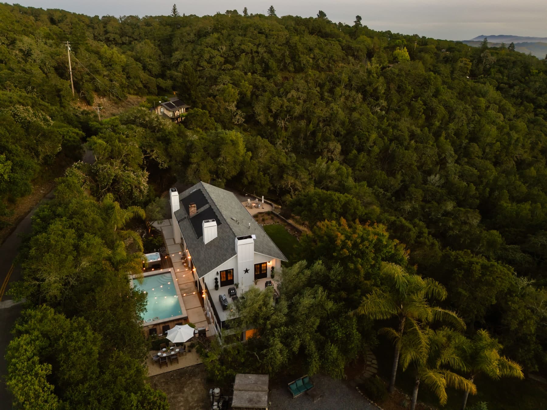 Aerial view of a dark-roofed villa with a pool surrounded by dense green trees