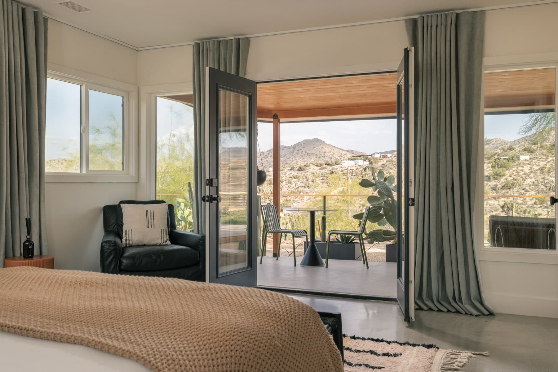 Bright bedroom opening through glass doors to a desert patio and mountain view